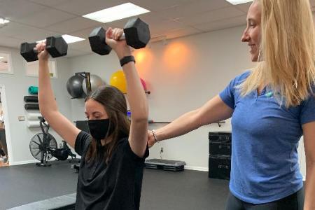 Physical therapist guiding patient who lifts dumbells